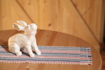 Table Runner, 2022, 9" x 32", Cotton and linen, Displayed alongside rabbit made by Wren Macdonald handwoven table runner with orange, blue, and white. Made on a shaft loom.